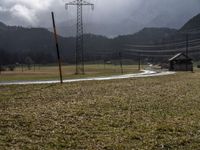 an empty field next to power lines on a cloudy day in the countryside with snow capped mountains