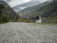 a gravel road with buildings under a grey sky and mountain background on a cloudy day