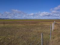 a large, empty field with some fence to protect it from falling grass in the distance is a long sky and large grassy field with clouds