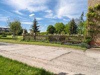 an empty garden with a fence and fenced in grass along the path with trees, bushes, and houses