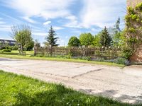 an empty garden with a fence and fenced in grass along the path with trees, bushes, and houses