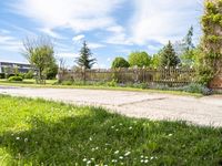 an empty garden with a fence and fenced in grass along the path with trees, bushes, and houses