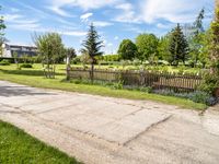 an empty garden with a fence and fenced in grass along the path with trees, bushes, and houses