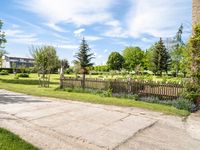 an empty garden with a fence and fenced in grass along the path with trees, bushes, and houses