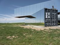 an abstract, mirrored structure on the outside of a building sitting in the grass in a field