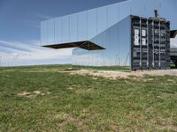 an abstract, mirrored structure on the outside of a building sitting in the grass in a field