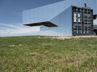 an abstract, mirrored structure on the outside of a building sitting in the grass in a field