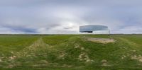 a strange reflection of a building in the middle of a field of grass near a cloudy sky