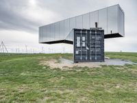 this container is surrounded by grass and wind mills it stands on a hill with a few trees