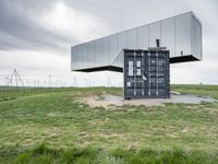 this container is surrounded by grass and wind mills it stands on a hill with a few trees