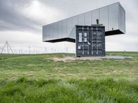 this container is surrounded by grass and wind mills it stands on a hill with a few trees