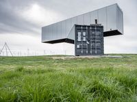 this container is surrounded by grass and wind mills it stands on a hill with a few trees