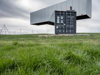 this container is surrounded by grass and wind mills it stands on a hill with a few trees