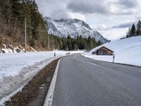 a road is lined with snow near a mountain range with forest covered in pine trees