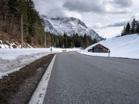 a road is lined with snow near a mountain range with forest covered in pine trees