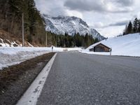 a road is lined with snow near a mountain range with forest covered in pine trees