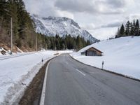 a road is lined with snow near a mountain range with forest covered in pine trees