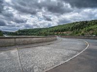 concrete walkway with trees and fenced in area on opposite sides of the road and one side of the road