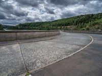 concrete walkway with trees and fenced in area on opposite sides of the road and one side of the road