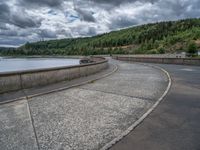 concrete walkway with trees and fenced in area on opposite sides of the road and one side of the road