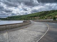 concrete walkway with trees and fenced in area on opposite sides of the road and one side of the road