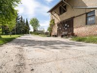 dirt road in front of a building with trees and grass around it, near by a bench