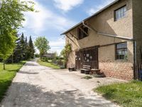 dirt road in front of a building with trees and grass around it, near by a bench