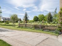 this is an empty street on a sunny day in the suburbs of ontario with trees, grass and a fence