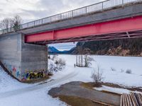 a bridge with a bunch of graffiti near water and snow in the area below it