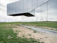 a large mirror sculpture on the side of the road next to windmills and grass