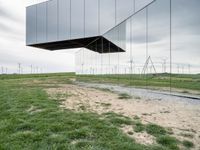 a large mirror sculpture on the side of the road next to windmills and grass