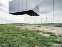 a large mirror sculpture on the side of the road next to windmills and grass