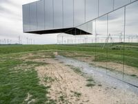 a large mirror sculpture on the side of the road next to windmills and grass