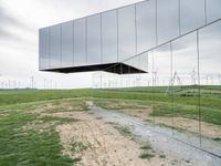 a large mirror sculpture on the side of the road next to windmills and grass