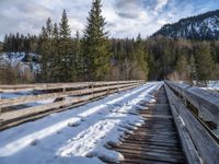 an old wooden bridge is covered in snow in the mountains above them are evergreen forest