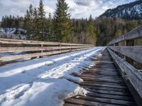 an old wooden bridge is covered in snow in the mountains above them are evergreen forest