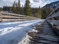 an old wooden bridge is covered in snow in the mountains above them are evergreen forest