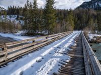 an old wooden bridge is covered in snow in the mountains above them are evergreen forest