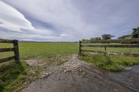 a grassy field that has a fence and a stream in the center of it and an open road next to it