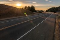 a long stretch of road at sunset with the sun behind a curve and trees on a hill in the foreground