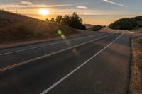 a long stretch of road at sunset with the sun behind a curve and trees on a hill in the foreground