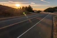 a long stretch of road at sunset with the sun behind a curve and trees on a hill in the foreground