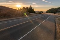 a long stretch of road at sunset with the sun behind a curve and trees on a hill in the foreground