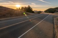 a long stretch of road at sunset with the sun behind a curve and trees on a hill in the foreground