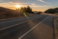 a long stretch of road at sunset with the sun behind a curve and trees on a hill in the foreground