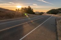 a long stretch of road at sunset with the sun behind a curve and trees on a hill in the foreground