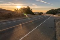 a long stretch of road at sunset with the sun behind a curve and trees on a hill in the foreground