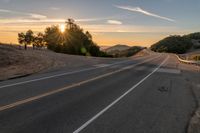 a long stretch of road at sunset with the sun behind a curve and trees on a hill in the foreground