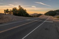 a long stretch of road at sunset with the sun behind a curve and trees on a hill in the foreground