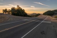 a long stretch of road at sunset with the sun behind a curve and trees on a hill in the foreground